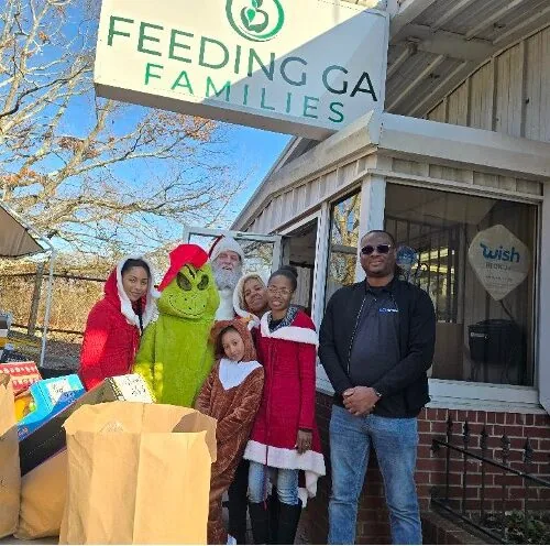 People in festive attire with a Grinch costume outside Feeding GA Families building, surrounded by donation bags