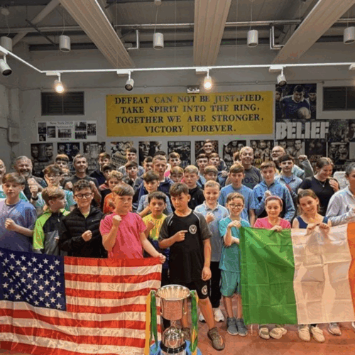 Group of people, including young boxers, holding USA and Ireland flags in a boxing club.