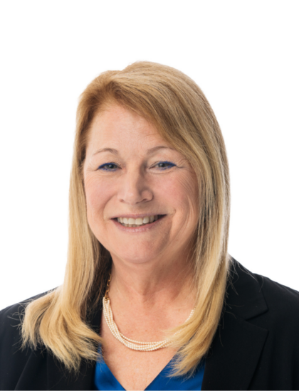 Lisa smiling, wearing a blue top, black blazer, and pearl necklace
