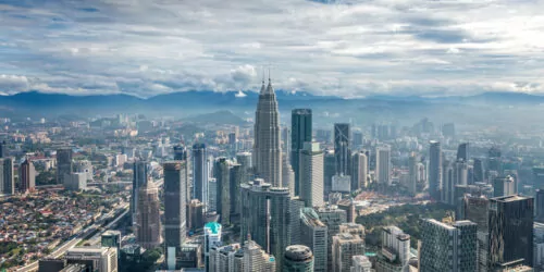 Kuala Lumpur skyline with Petronas Towers under a cloudy sky.