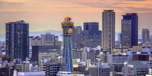 Osaka skyline at sunset featuring Tsutenkaku Tower and surrounding skyscrapers.
