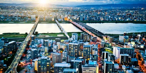 Aerial view of a vibrant cityscape in Osaka, Japan, at sunset, with bridges spanning a river and illuminated buildings
